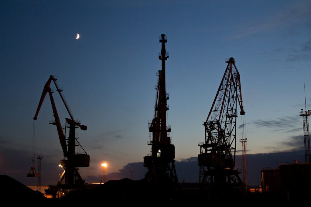 Oil port cranes silhouetted against a twilight sky with a crescent moon, highlighting industrial oil operations at dusk.