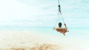 A man is sitting on a swing on a tropical island