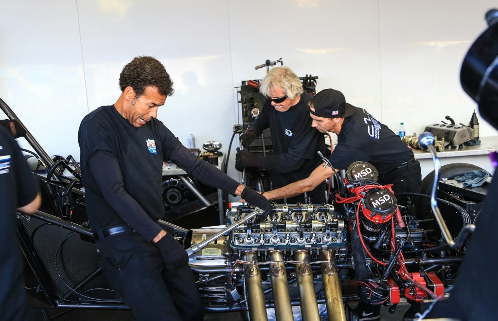 Three mechanics working together on a high-performance engine in a garage.
