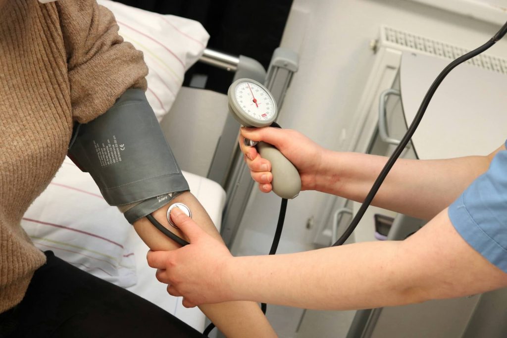 Healthcare worker measuring a patient's blood pressure using a manual sphygmomanometer and stethoscope.