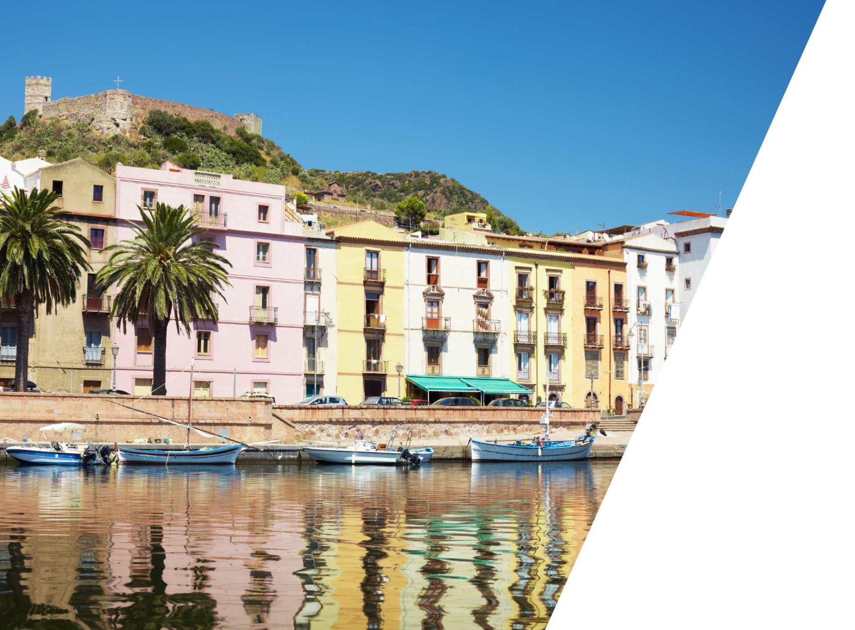 Colorful houses along a canal in Sardinia, with a castle on a hill in the background.