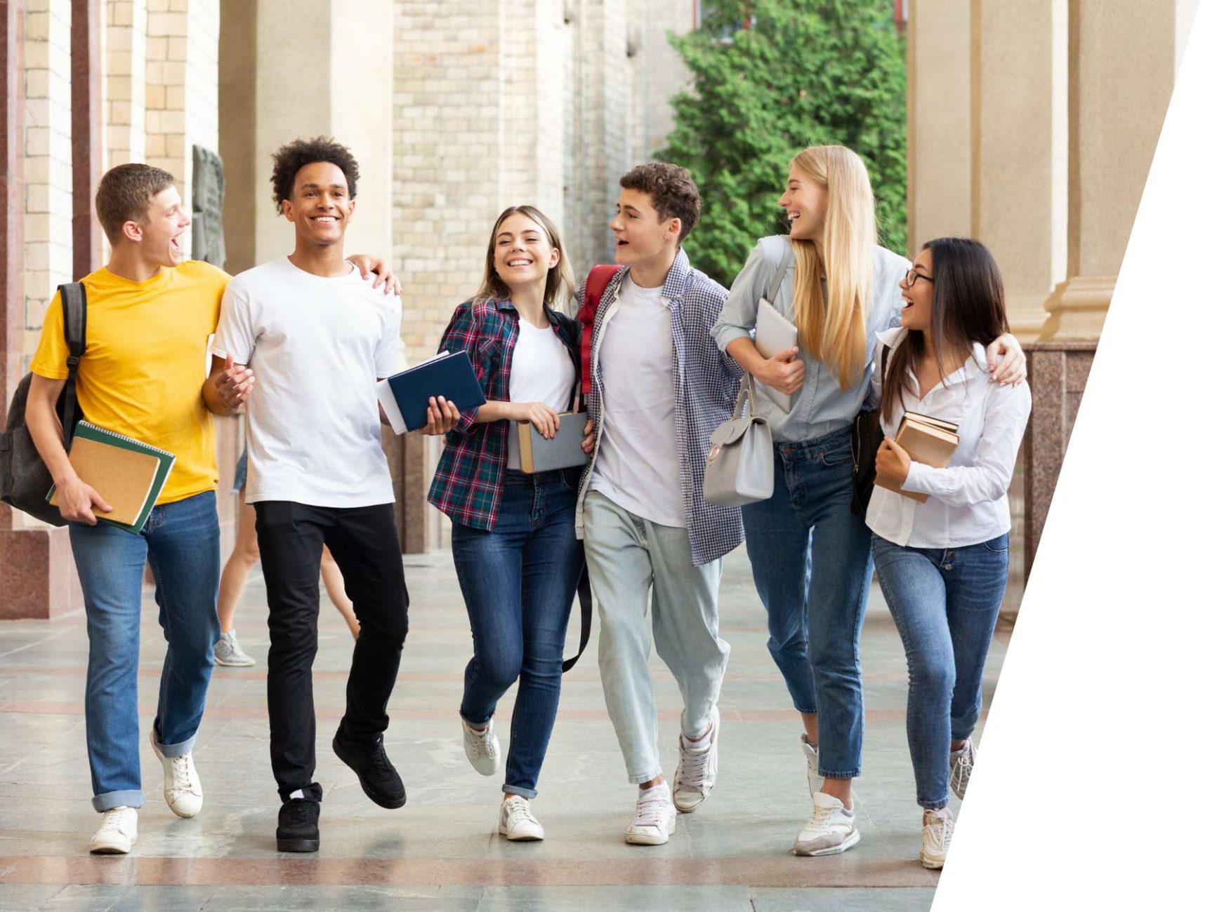 A group of six students laughing and conversing. In the background, there are sandstone-colored columns of a building and a tree.