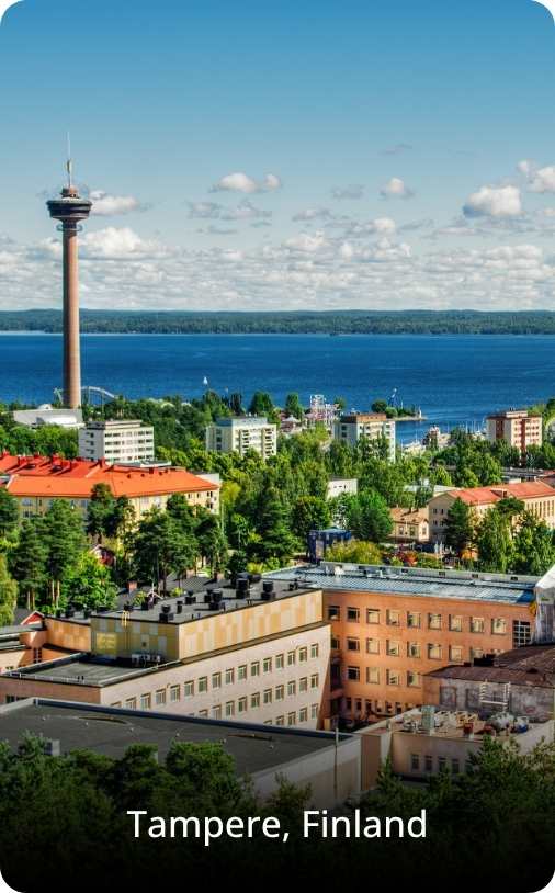 Scenic view of Tampere, Finland, featuring red brick industrial buildings and modern university structures along a calm river, with greenery and blue sky above. Ideal for students exploring study abroad in Tampere, the image highlights the city’s blend of nature, architecture, and academic atmosphere.