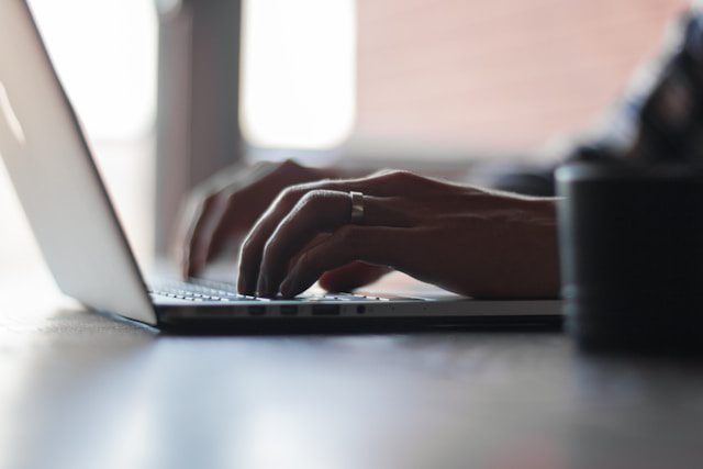Close-up of hands typing on a laptop keyboard in a softly lit workspace with a blurred mug in the foreground.