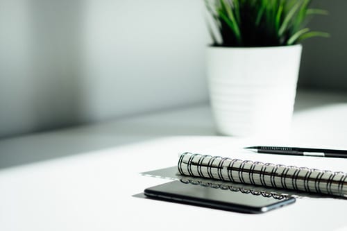notebook, phone and a pen laying on a white table