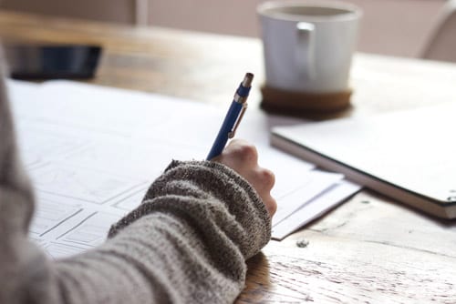 man wearing a long sleeve is writing on a notebook