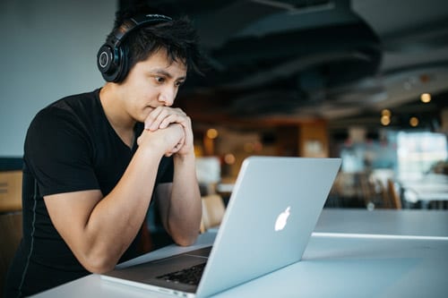 a guy in black shirt wearing headphones is looking at a laptop