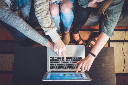 three people pointing at a screen of a laptop