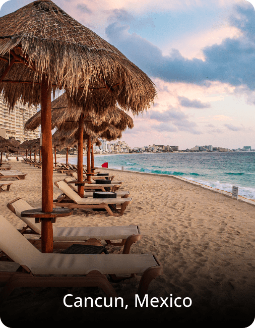 Beach in Cancun, Mexico, with rows of sunbeds on white sand and turquoise water under a cloudy sky.