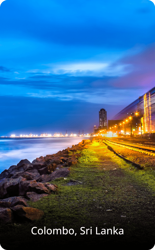 Night view of the coastline in Sri Lanka, with calm waves and distant lights reflecting on the water under a dark sky.