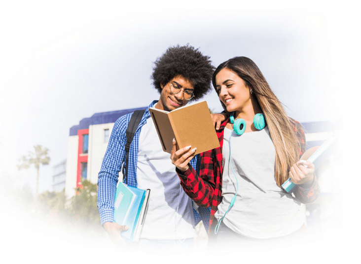 Two students standing side by side, smiling as they read a book together in a casual academic setting.