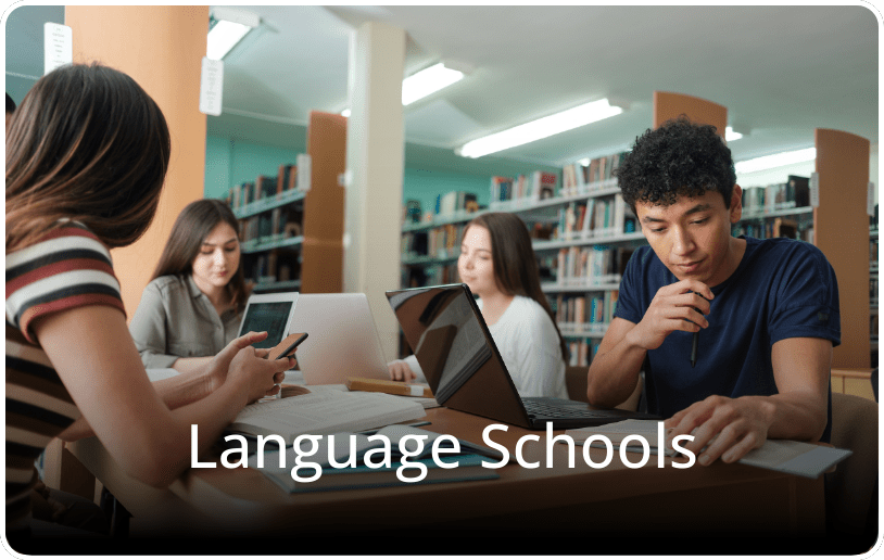 Four students sitting in a library with laptops, studying together, with the text “Language Schools” overlaid on the image.