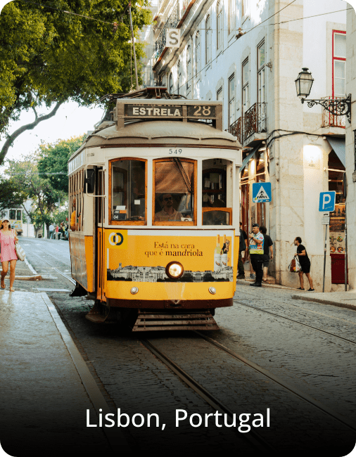 Iconic Tram 28 in Lisbon, Portugal, traveling through a narrow street lined with colorful buildings and cobblestone pavement.