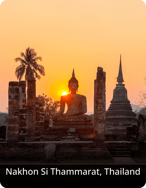 Silhouette of a Buddha statue and temple ruins at sunset in Nakhon Si Thammarat, Thailand, surrounded by palm trees.