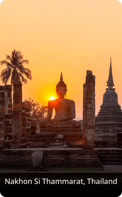 Silhouette of a Buddha statue and temple ruins at sunset in Nakhon Si Thammarat, Thailand, surrounded by palm trees.