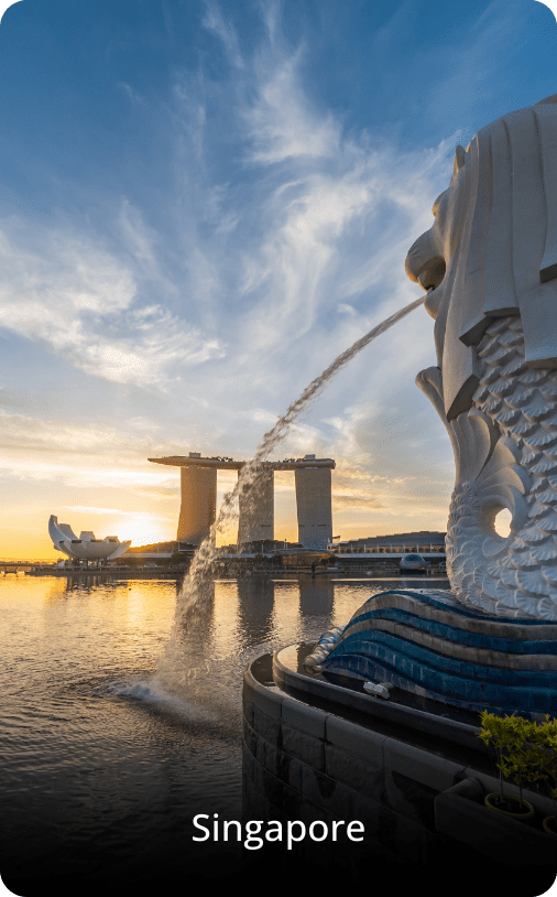 Sunset view of Singapore with the Merlion fountain in the foreground and Marina Bay Sands' triple skyscraper in the background.