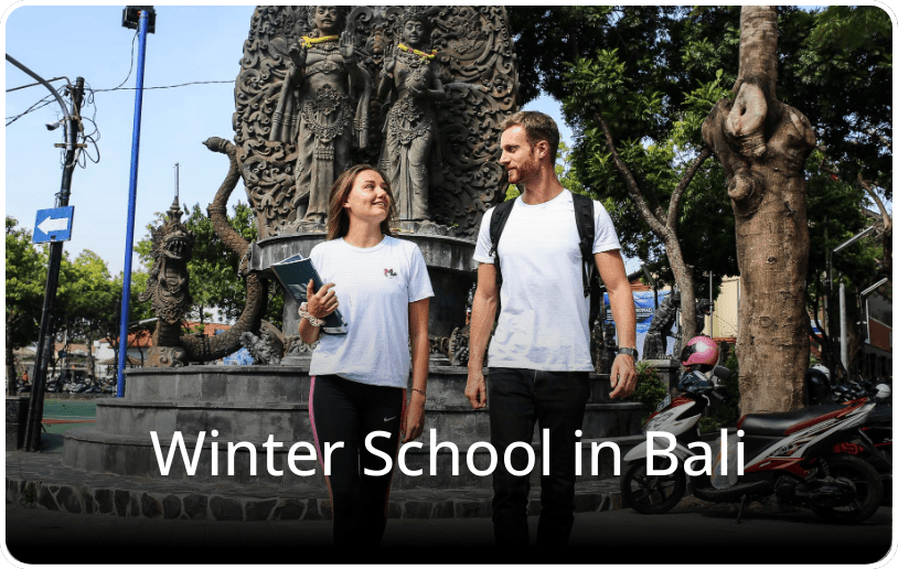 Two students walking and talking in an urban area in Bali, with the text “Winter School in Bali” overlaid on the image.