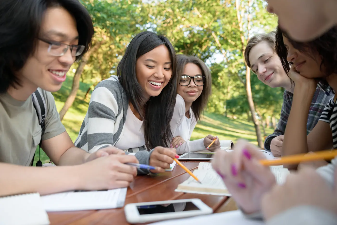 Students sitting around a table outdoors, studying and smiling together in a relaxed and collaborative setting.